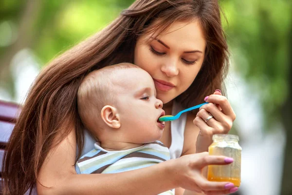 Bebé cuchara de alimentación por la madre en el parque al aire libre. El destete  . — Foto de Stock