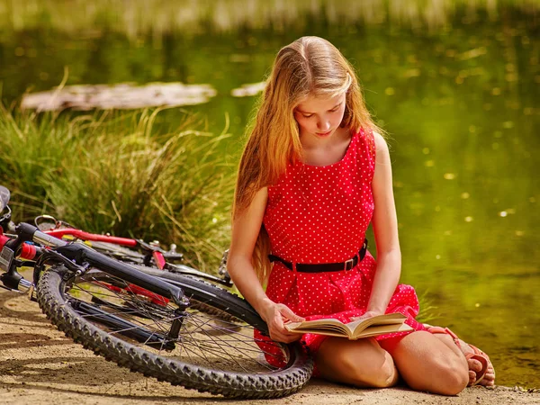 Fille en vélo livre de lecture près de vélo dans le parc en plein air . — Photo
