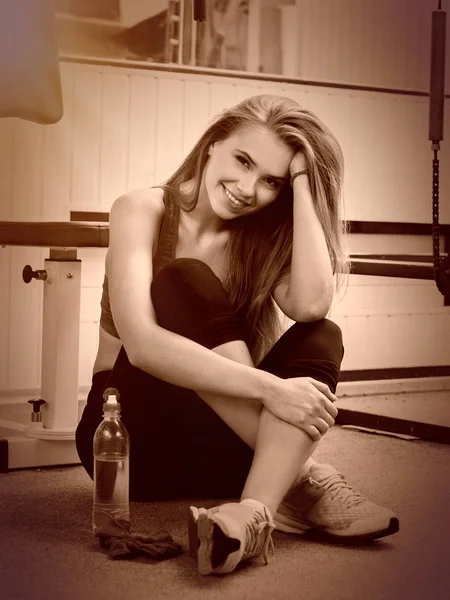 Women drink water at gym. Girl resting after training at sport room.