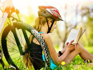 Kask giyen kız Bisiklete binme Bisiklet Bisiklet yakınındaki diğer kitap okumak.