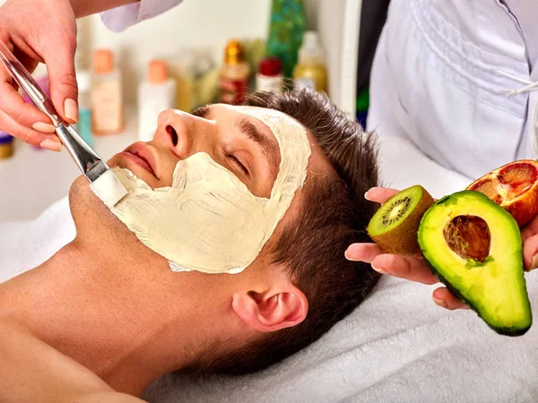 Facial mask from fresh fruits for man . Beautician apply slices.