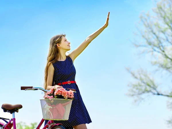 Menina vestindo bolinhas azuis passeios de sundress bicicleta com flores cesta . — Fotografia de Stock