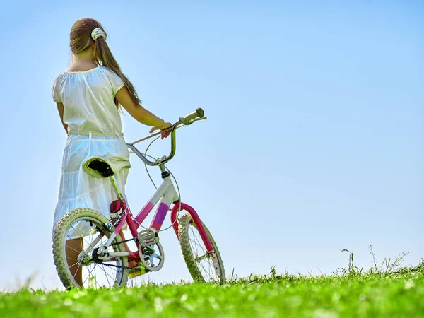 Child girl wearing white skirt rides bicycle into park. — Stock Photo, Image