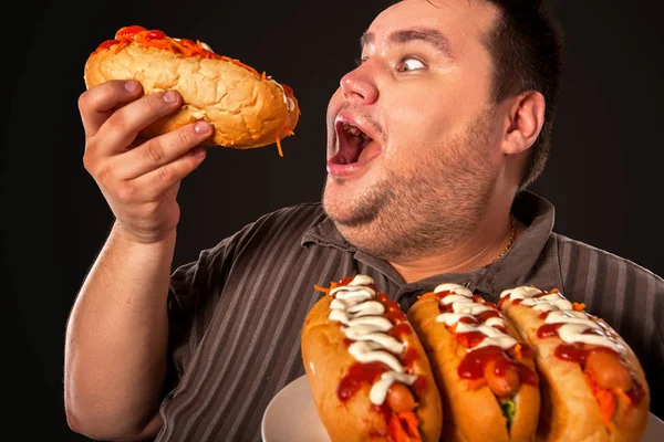 Hombre gordo comiendo perritos calientes de comida rápida. Desayuno para personas con sobrepeso . — Foto de Stock