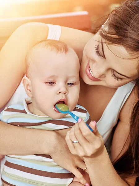 Madre nutrire il suo porridge bambino da cucchiaio all'aperto nel parco . — Foto Stock