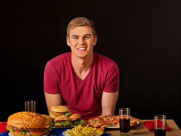 Mężczyzna jedzenie hamburgerów, pizzy i talerz frytek. — Zdjęcie stockowe