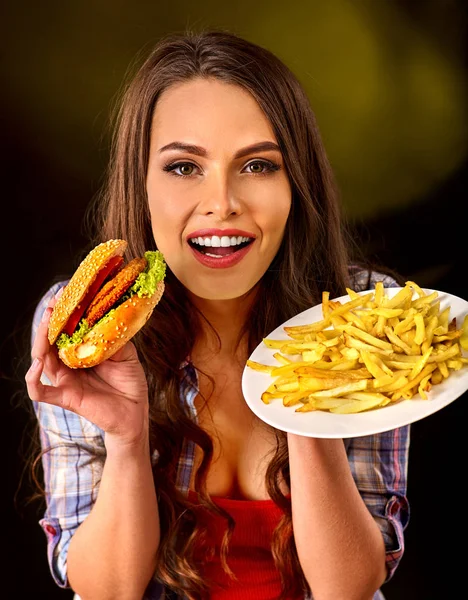 Woman eating french fries and hamburger on table.