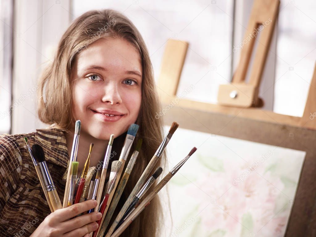 Artist painting on easel in studio. Girl paints with brush.