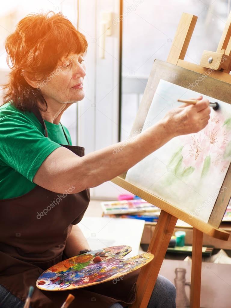 Artist painting easel in studio. Authentic senior woman.