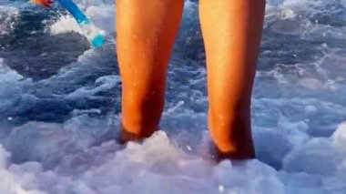 Deniz köpüğü dalgası altında çıplak ayaklı bir kızın plaj tatili