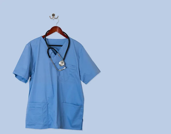 Blue scrubs shirt for medical professional hanging on blue wall — Stock Photo, Image