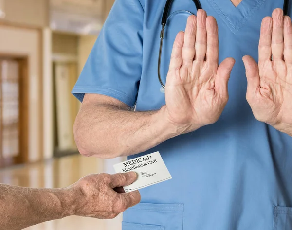 Senior doctor in scrubs refusing Medicaid Card — Stock Photo, Image