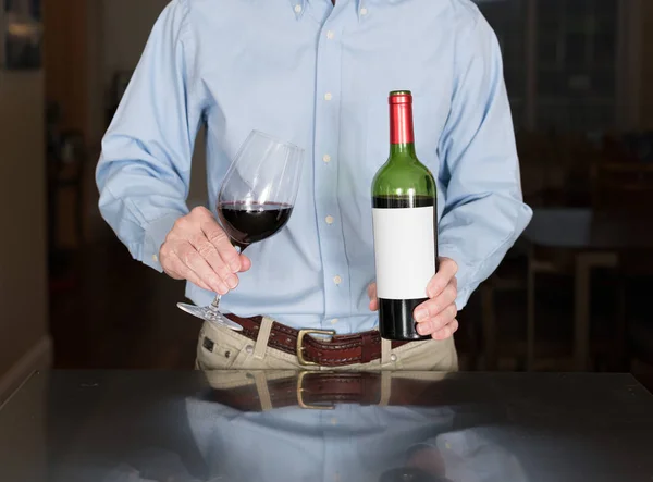 Senior gießt aus Weinflasche mit leerem Etikett — Stockfoto