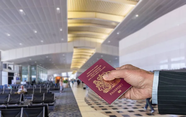 Braço executivo sênior segurando passaporte do Reino Unido no terminal do aeroporto — Fotografia de Stock