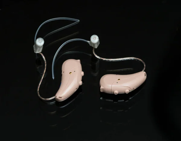 Zbliżenie na parę drobnych nowoczesnych aparatów słuchowych na czarnym tle — Zdjęcie stockowe