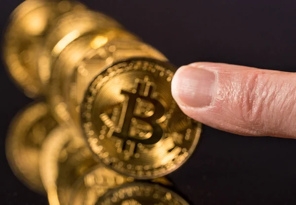 Bitcoin-Münzen in einer Reihe auf reflektierender Oberfläche mit dem Finger, um sie zu drücken — Stockbild Bitcoins stehen in einer Reihe wie Dominosteine mit dem Finger — Stockfoto