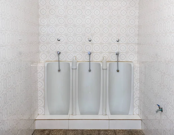 Tres urinarios de longitud completa en una fila en un baño de azulejos o pared del baño —  Fotos de Stock