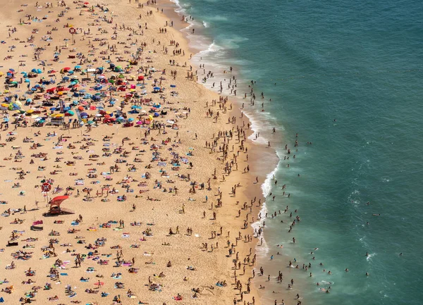 Vista aérea de los turistas en la playa nazarí en Portugal el día de verano lleno de gente —  Fotos de Stock