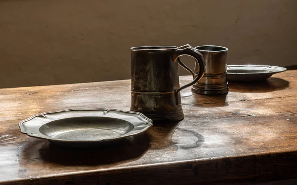 Retro stijl tinnen mokken en borden op grote houten eettafel — Stockfoto