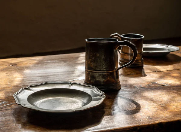 Canecas de pewter estilo retro e placas em grande mesa de jantar de madeira — Fotografia de Stock