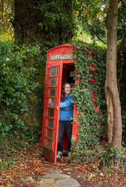 Klasická červená telefonní budka v anglickém venkově se ženou vychází — Stock fotografie