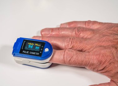 Yaşlı adam kan oksijeni seviyesini ölçmek için parmakta nabız oksimetresi kullanıyor.
