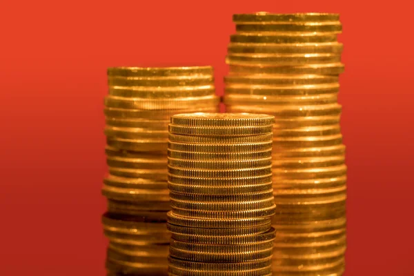 Gold coins stacked with other piles in the background out of focus with a red backdrop — Stock Photo, Image