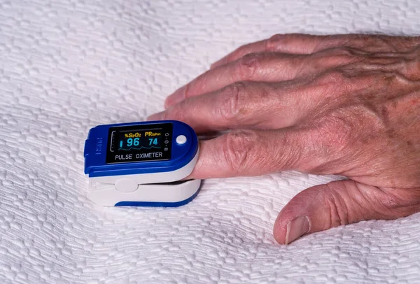 Старший чоловік використовує імпульсний оксиметр на пальці для перевірки рівня кисню в крові — стокове фото
