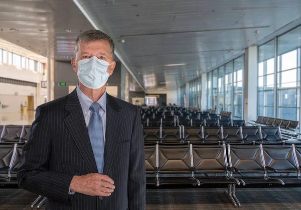Senior adult businessman wearing a face mask against coronavirus in airport terminal — Stock Photo, Image