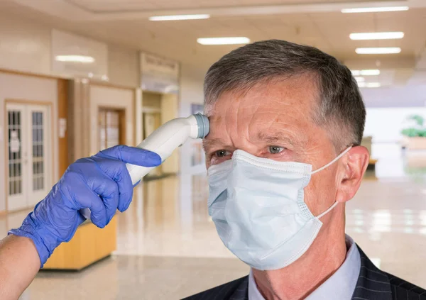 Senior mand iført ansigtsmaske med temperatur taget for at kontrollere for virus på hospitalet - Stock-foto