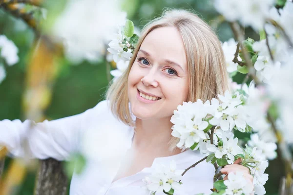Улыбающаяся взрослая женщина с цветком в весеннем саду — стоковое фото