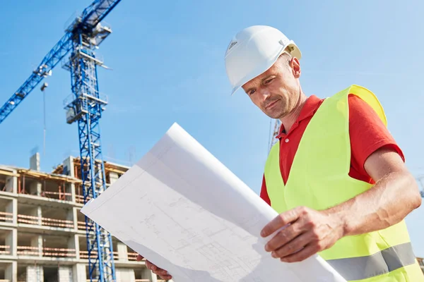 Obrero de la construcción con plano en el área del edificio Imagen de stock