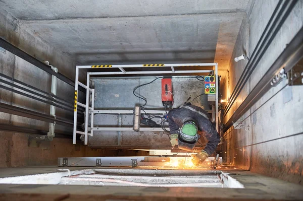 Lift worker welding elevator fasteners in lift shaft — Stock Photo, Image