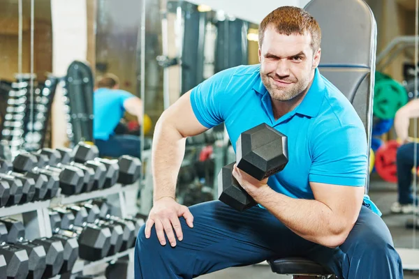 Cheerful fitness bodybuilding trainer with dumbbell at gym