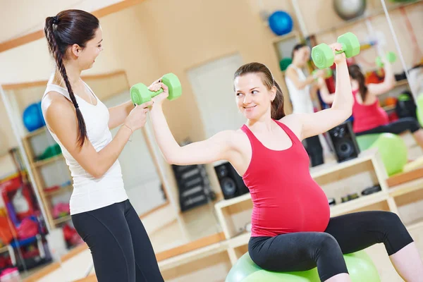 Mujer embarazada con instructor haciendo ejercicio de pelota de fitness —  Fotos de Stock