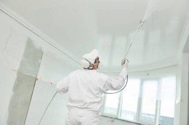 Painter worker with airless painting sprayer covering ceiling surface into white clipart