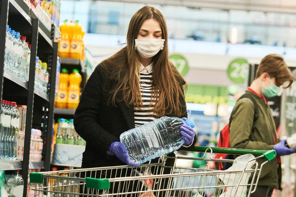 Hombre con máscara y guantes de protección comprar tienda de agua en coronavirus epidemia —  Fotos de Stock