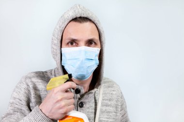 Kafkasyalı maskeli beyaz adam Coronavirus 'ten korumak için temiz sprey tutuyor. Covid-19 salgını, gri arkaplan, kopyalama alanı