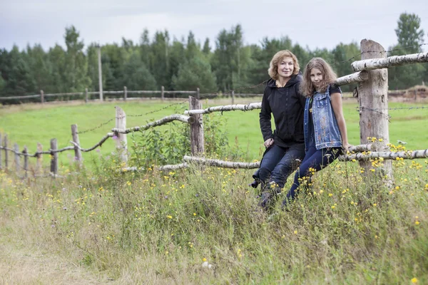 田舎の成熟した母と10代の娘の肖像画 牧草地の木製の柵の上に一緒に座って 女性農家 コピースペース — ストック写真
