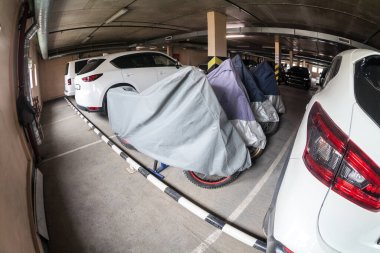 Plastik çarşafla kaplı motosikletler yeraltı garajında park edilmiş. Motosikletler bir otopark satışıyla ayakta duruyor.