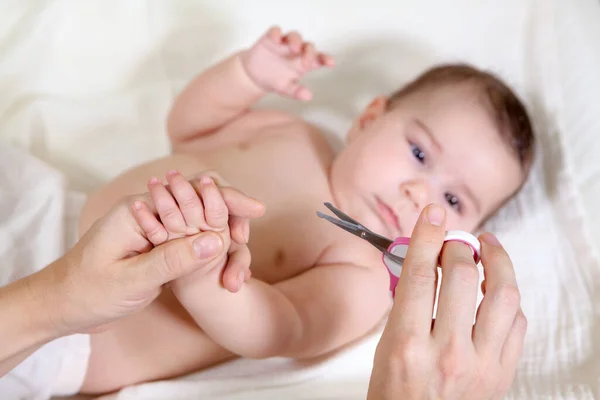 母親保持小さな指の彼女の赤ちゃんのために切断はさみ 白人の幼児ベッドの上に横たわる — ストック写真
