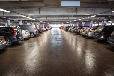 Arabalar çok katlı bir otoparkta, her yer dolu, araçların üstünde kırmızı ışıklar var.