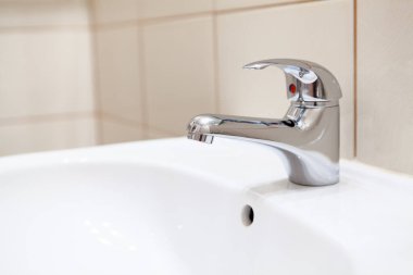 Beyaz banyo lavabosunda paslanmaz su musluğu.