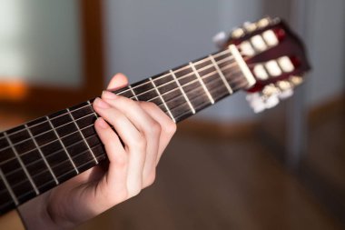 Akustik gitar fretboard 'u. Dişi uzun parmakları akora vuruyor.