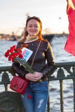 Elinde kırmızı karanfiller olan genç Rus kadının portresi, 2. Dünya Savaşı 'ndaki Zafer Günü' nün 70. yıldönümünü kutluyor. St. Petersburg, Rusya. Bayrak üzerine Rusça metin: Zafer 70 yıl