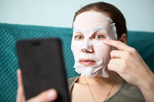 Mujer Joven Caucásica Aplicando Mascarilla Rejuvenecedora Facial Usando Teléfono Inteligente —  Fotos de Stock