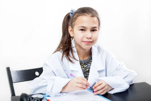 Ragazza Allegra Età Scolare Cappotto Medico Bianco Siede Tavolo Uno — Foto Stock