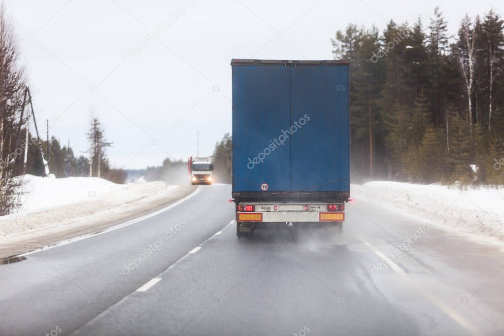 Rear view at semitrailer truck driving on slippery winter road in northern forest