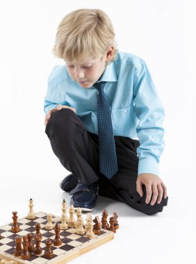 Genç bir çocuk iş stili kıyafetler yerde satranç oynuyor, beyaz arka planda bir kişi.