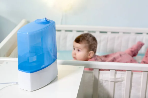 使用中の加湿器とベビーベッドの上に寝そべっている赤ん坊の女の子 自宅で呼吸器疾患予防 — ストック写真